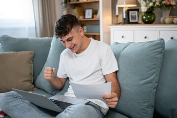 Happy student celebrating success with laptop and documents on sofa