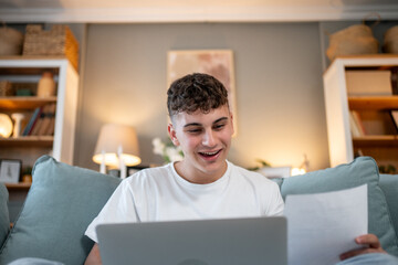 Happy student studying online and reading notes on sofa at home