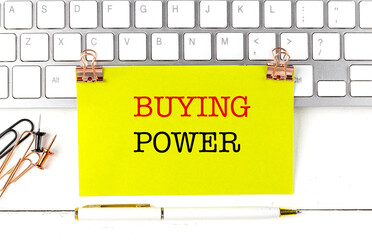 Yellow note with the words buying power clipped to keyboard with office supplies and pen