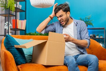 Angry dissatisfied shopper Indian man unpacking parcel feeling upset and confused with wrong...