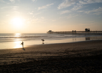 Surfers carrying surfboards at sunset on the sandy beaches of Oceanside California near the...