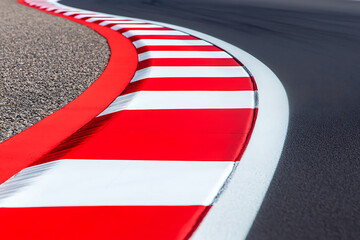 High-angle view of a racetrack corner with red and white safety curbs and black tarmac. The smooth pavement contrasts with the gravel on the outside edge.