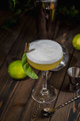 Refreshing yellow cocktail garnished with lime and leaf on wooden table