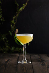 Refreshing yellow tropical cocktail garnished with leaf on wooden table