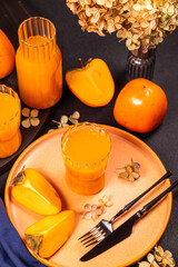 Fresh persimmon juice with ripe fruits and dried flowers on table