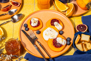 Sliced persimmon with ricotta, blood orange and blueberries on colorful table setting