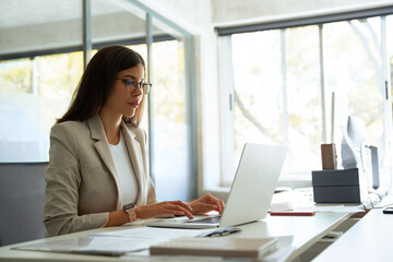 Focused middle aged business woman using laptop at work in office. Professional female executive entrepreneur in suit working on computer pc at company workplace, doing financial analyze. Copy space