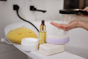 Spa essentials and shower water flowing over hand, modern bathroom self-care skincare routine.
