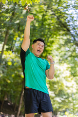 Obraz premium Athletic fit runner guy celebrate success win scream rejoices triumph victory marathon race. Workout cardio training in sunny park. Asian young man enjoy healthy lifestyle. Active sportsman motivation
