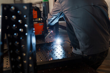 Welder meticulously joins metal components on a welding table, utilizing specialized equipment and...