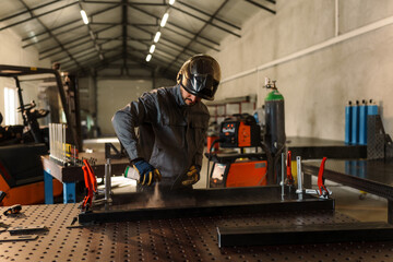 Metalworker wearing protective gear and cleaning a welding table with a spray in a workshop, with...