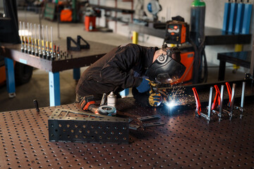Professional metalworker wearing protective gear welding metal part on workbench using specialized...