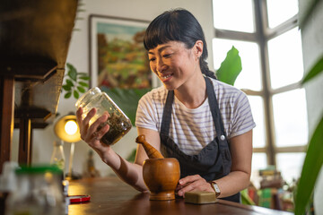 japanese woman use herbs from jar to make homemade products at workshop