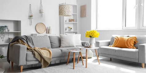 Soft sofa, coffee table and bouquet of narcissus flowers in light living room