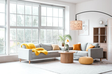 Interior of light living room with cozy grey sofas, coffee table and glowing lamps near big window