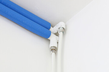 Insulated water pipes system. Blue foam thermal cover. White plumbing tubes in corner. Central heating installation view. Indoor pipe connection detail. Modern home energy saving solution.