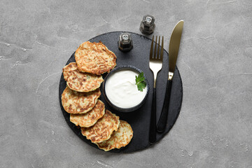 Board of tasty zucchini fritters with sour cream on grey background