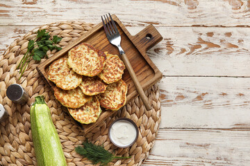 Board of tasty zucchini fritters with sour cream on light wooden background
