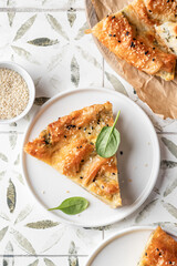 Greek pie spanakopita with feta cheese and spinach on a white plate on printed tile background top view