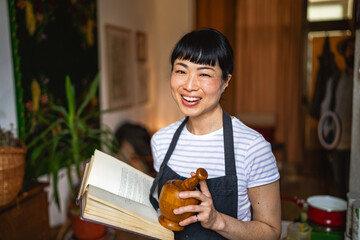 mature japanese woman hold mortar, book and pestle at herbal workshop