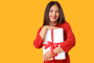 Beautiful young Asian woman with gift box on yellow background
