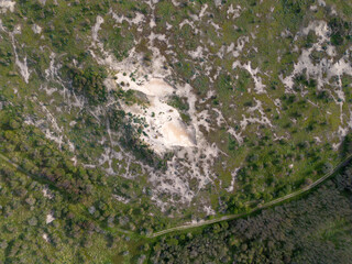 Aerial view of a sandy area surrounded by green vegetation and trees, showcasing a natural landscape with patches of grass and shrubs, captured from a drone.