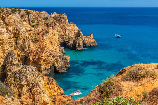 Beautiful cove with clear blue sea, boats and golden cliffs The Algarve Portugal

