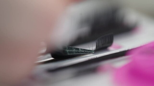 Extreme close-up of tweezers gripping individual eyelash extensions from a tray, preparing for lash application in a beauty treatment setting.
