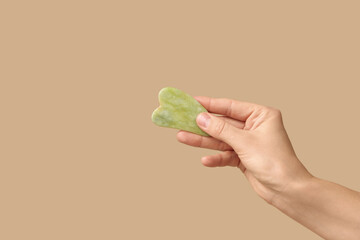 Female hand with guasha massage tool on beige background