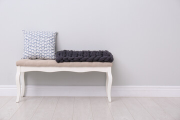 Knitted merino wool plaid and pillow on bench near grey wall