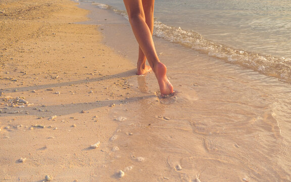 Rear view low section of a barefoot teenage girl walking on a beach, Bali, Indonesia