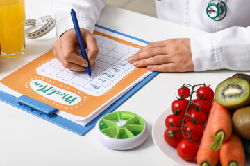 Young female nutritionist with healthy food writing diet plan in office, closeup