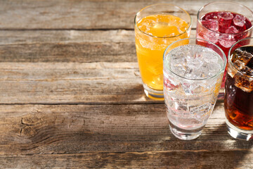 Soda water of different flavors with ice cubes in glasses on wooden table, closeup. Space for text