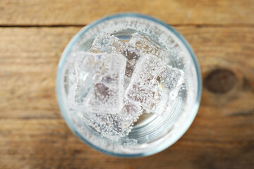 Refreshing soda water with ice cubes in glass on wooden table, top view