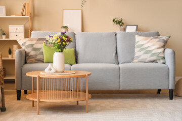 Comfortable sofa and wild flowers in vase on coffee table in living room