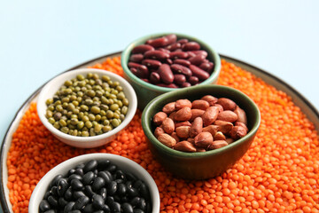 Bowls with raw legumes on color background, closeup