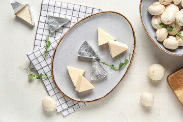 Plate with triangles of tasty processed cheese, mushrooms and napkin on light background