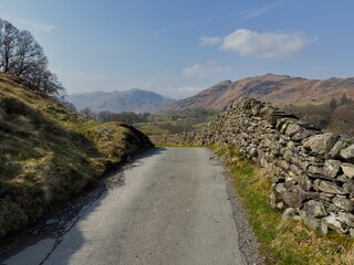 Narrow country lane bordered by dry stone walls with views of distant Lake District hills in spring