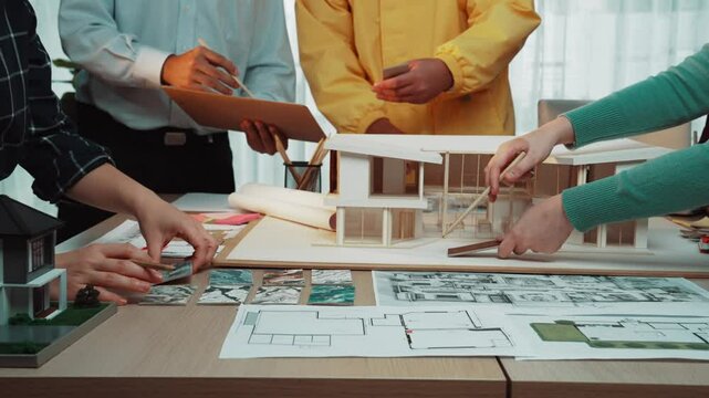 A diverse team of architects collaborates in a modern office, discussing design ideas and analyzing blueprints while surrounded by building models and documents. SACTR