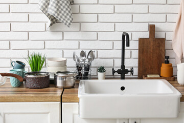 Ceramic sink and clean dishes on wooden counter near light brick wall