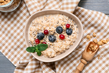 Napkin, bowl with tasty oatmeal, chia seeds and berries on grey wooden background