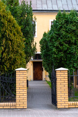 Naklejka premium Wejście do posesji z otwartą bramą i drzewami – Przestrzeń miejska z zielenią w tle.