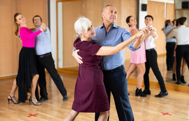 Happy aged woman learning to dance Vienneze waltz with partner in dancing class. Active hobby of older generation concept