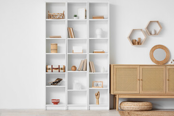 Interior of light living room with wooden commode and shelves