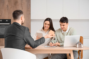 Young couple signing house rental agreement with real estate agent at table in kitchen