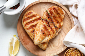 Wooden plate with tasty grilled chicken breast, thyme, peppercorns and lemon slice on white background