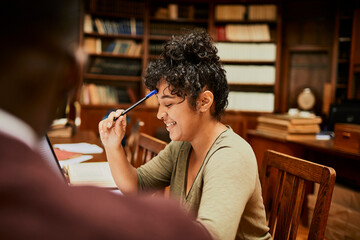 Happy female student studying in library sitting at desk with open book and pen in hand