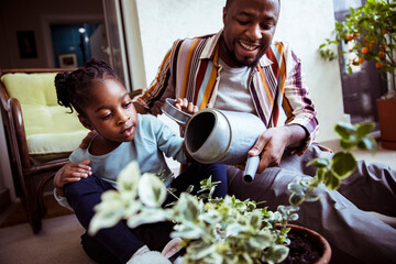 Father and daughter watering plants and flowers on the balcony of their apartment
