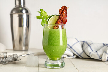 Glass of bloody Mary cocktail garnished with bacon, lime and celery on white tile table