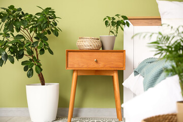Bedside table with houseplants and wicker basket near bed